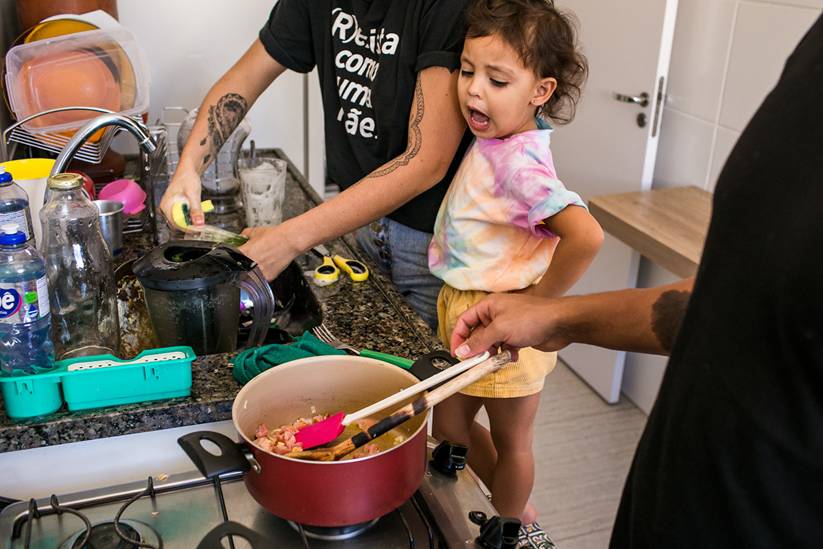 Criança sobe no banco da cozinha para ajudar aos pais a preparar o almoço, em foto de Adriana Costa
