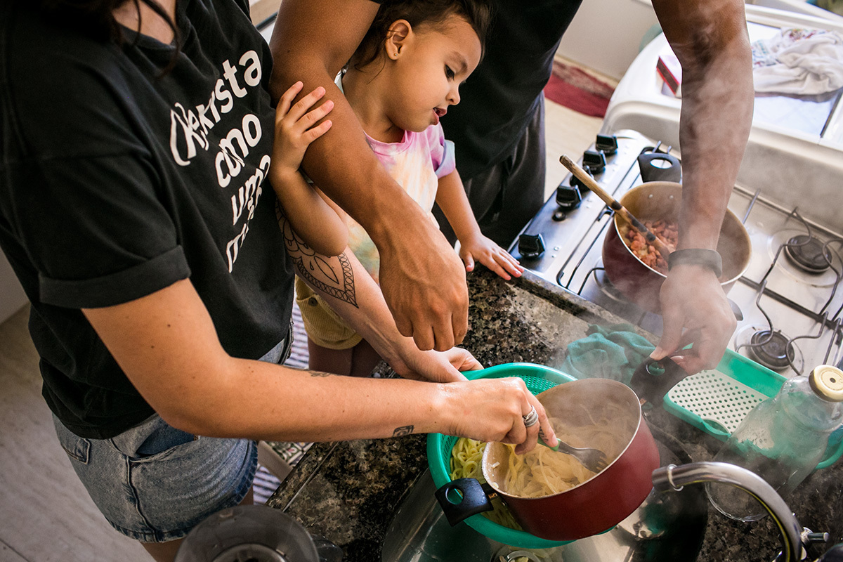 Foto de Adriana Costa dos pais e filha de 3 anos preparando juntos a macarronada para o almoço 