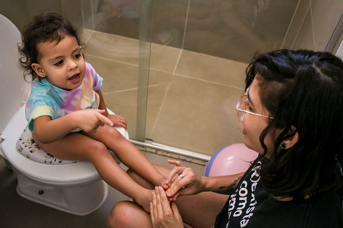 mãe faz massagem nos pés da filha enquanto ela está no vaso sanitário