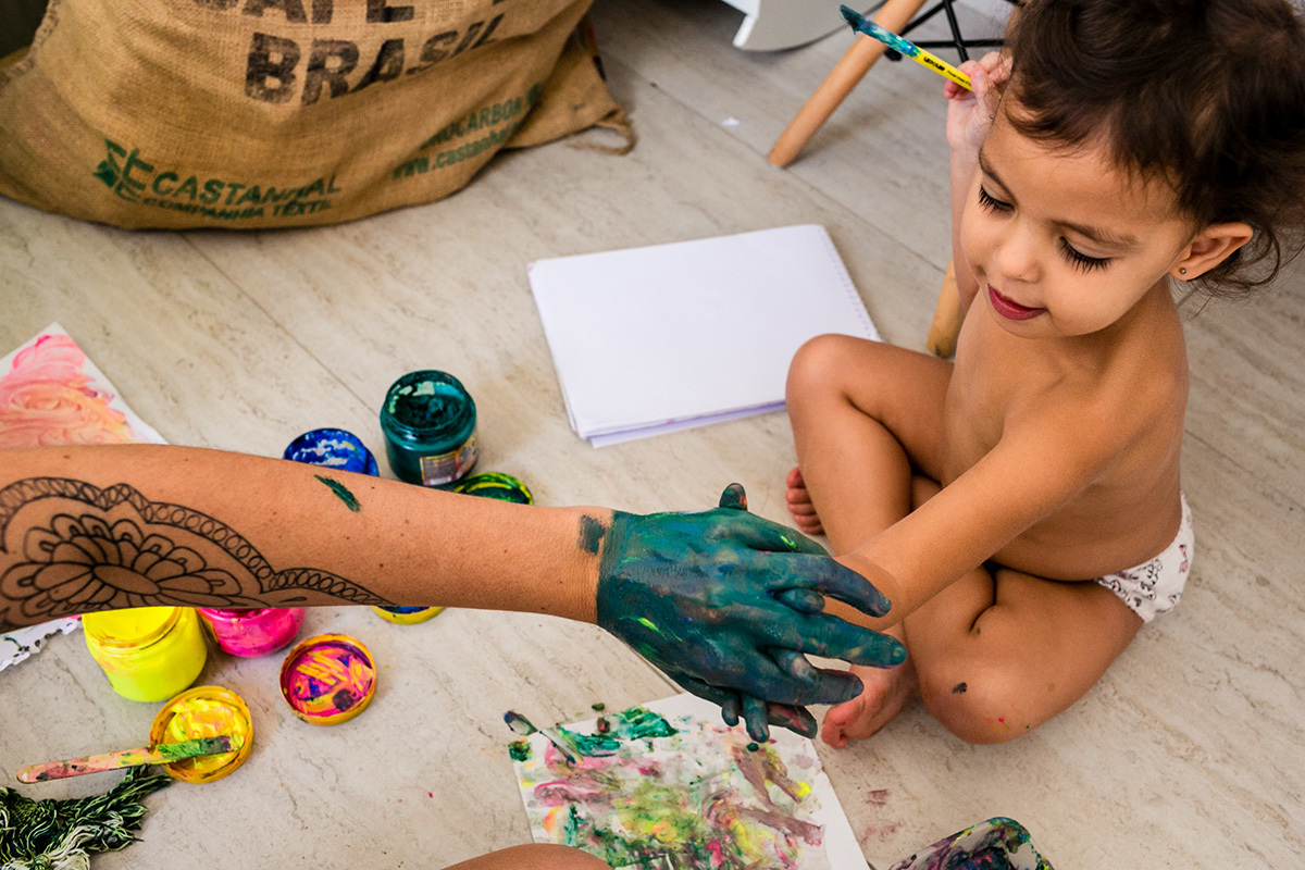 mãe e filha entrelaçam as mão que estão cheias de tinta