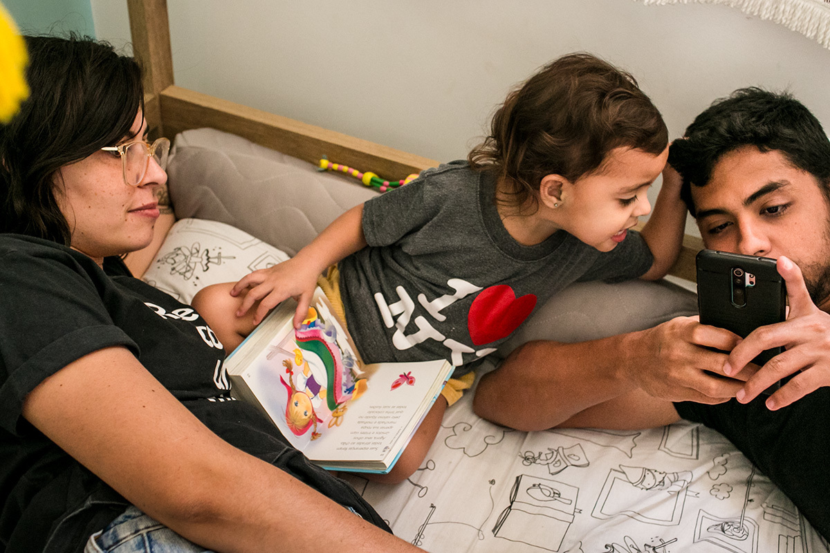 menina chama a atenção do pai que está no celular para ler um livro com ela.