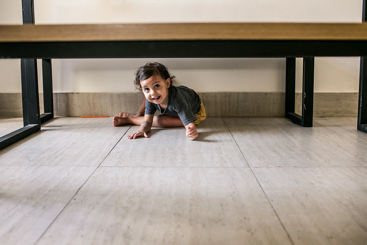 menina se diverte escondendo debaixo da mesa, em foto de Adriana Costa