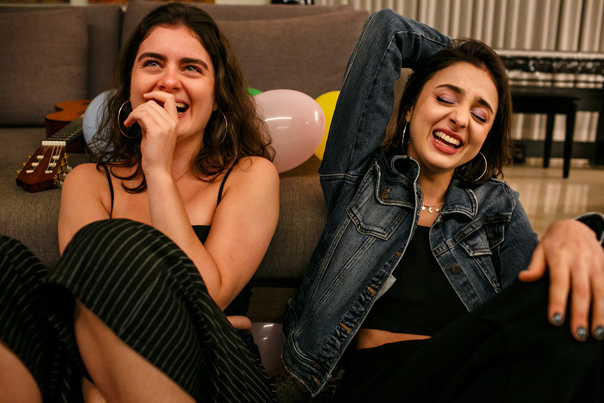 irmãs dão gargalhadas juntas durante a festa de aniversário feita em casa devido a pandemia, em foto de Adriana Costa