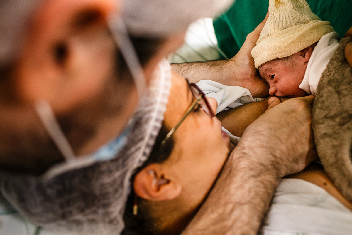 marido ajuda esposa a amamentar logo após o nascimento em foto de Adriana Costa