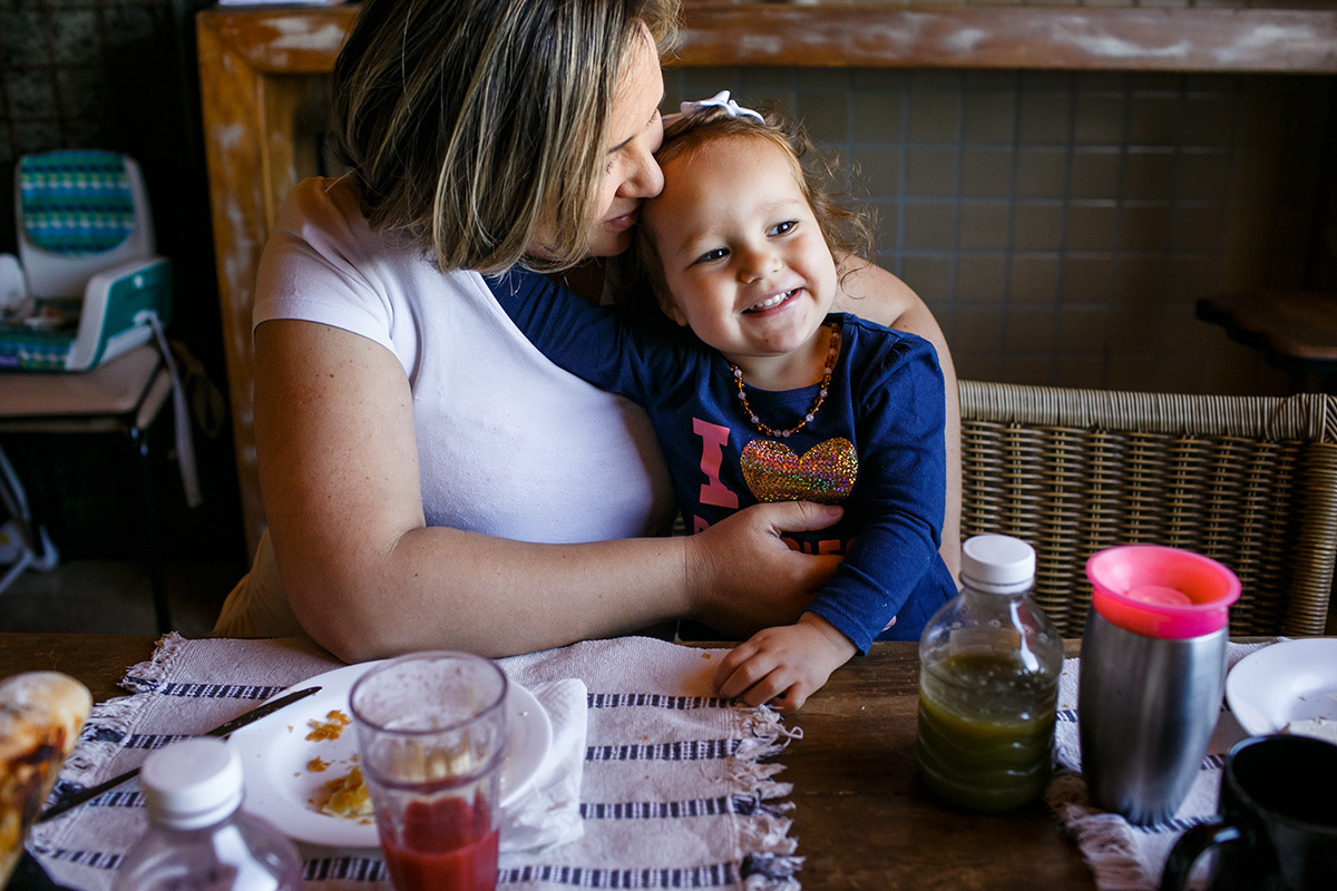 mãe grávida abraçada a sua outra filha em foto de Adriana Costa durante o café da manhã
