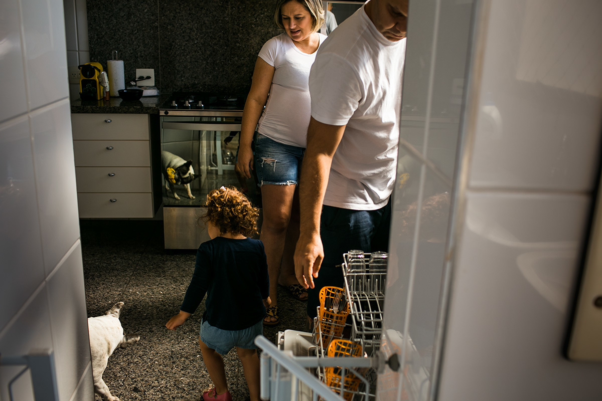 criança brinca com o cachorro enquanto sua mãe gravida e seu pai arrumam a cozinha