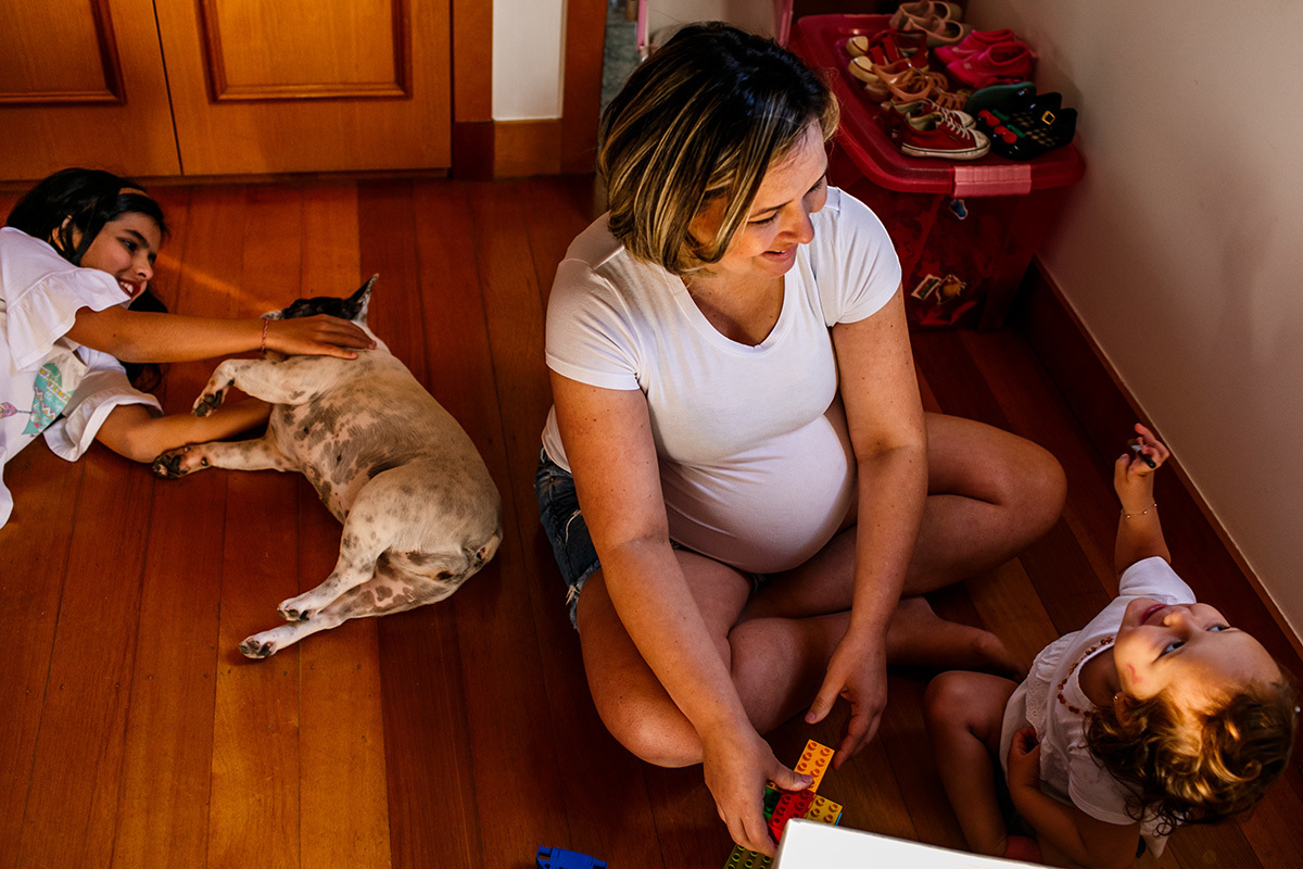 mãe gravida brincando com suas filhas e o cachorro no quarto