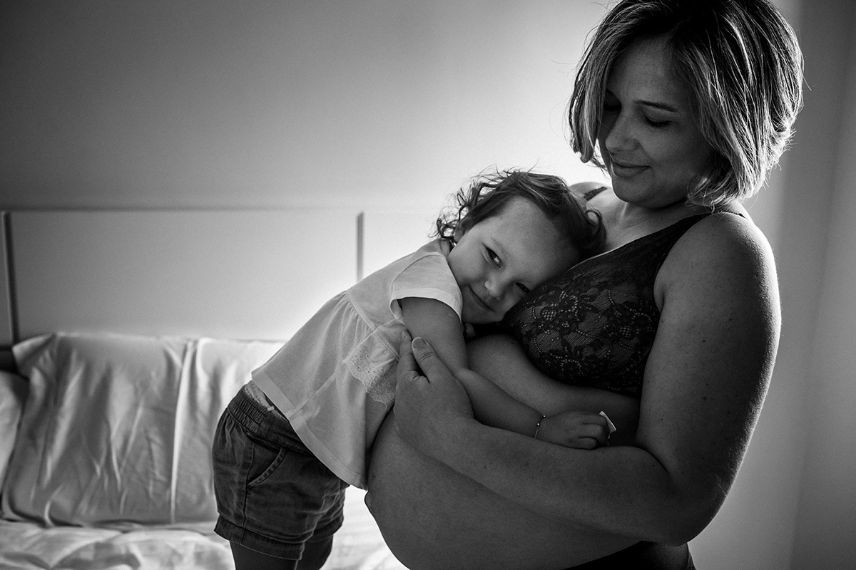 criança abraça carinhosamente a barriga da mãe grávida em foto de Adriana Costa