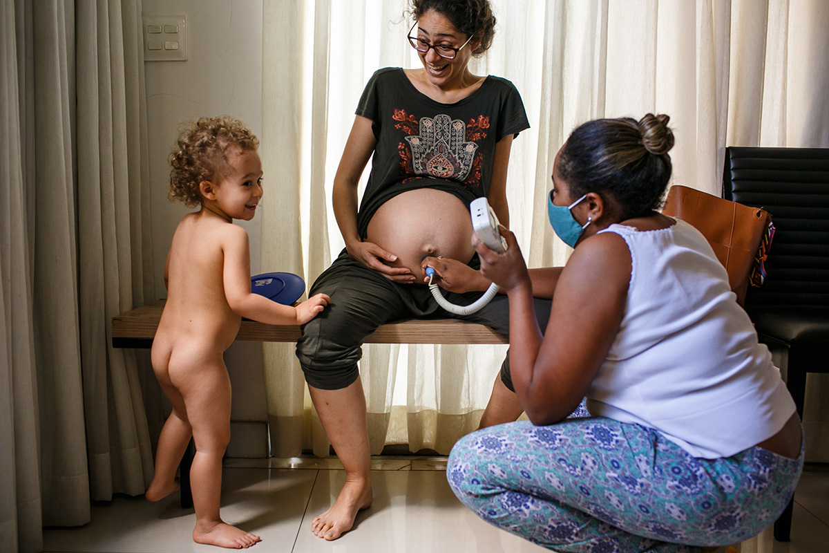Adriana costa fotografou gestante sendo avaliada durante um parto domiciliar ao lado de seu primogênito