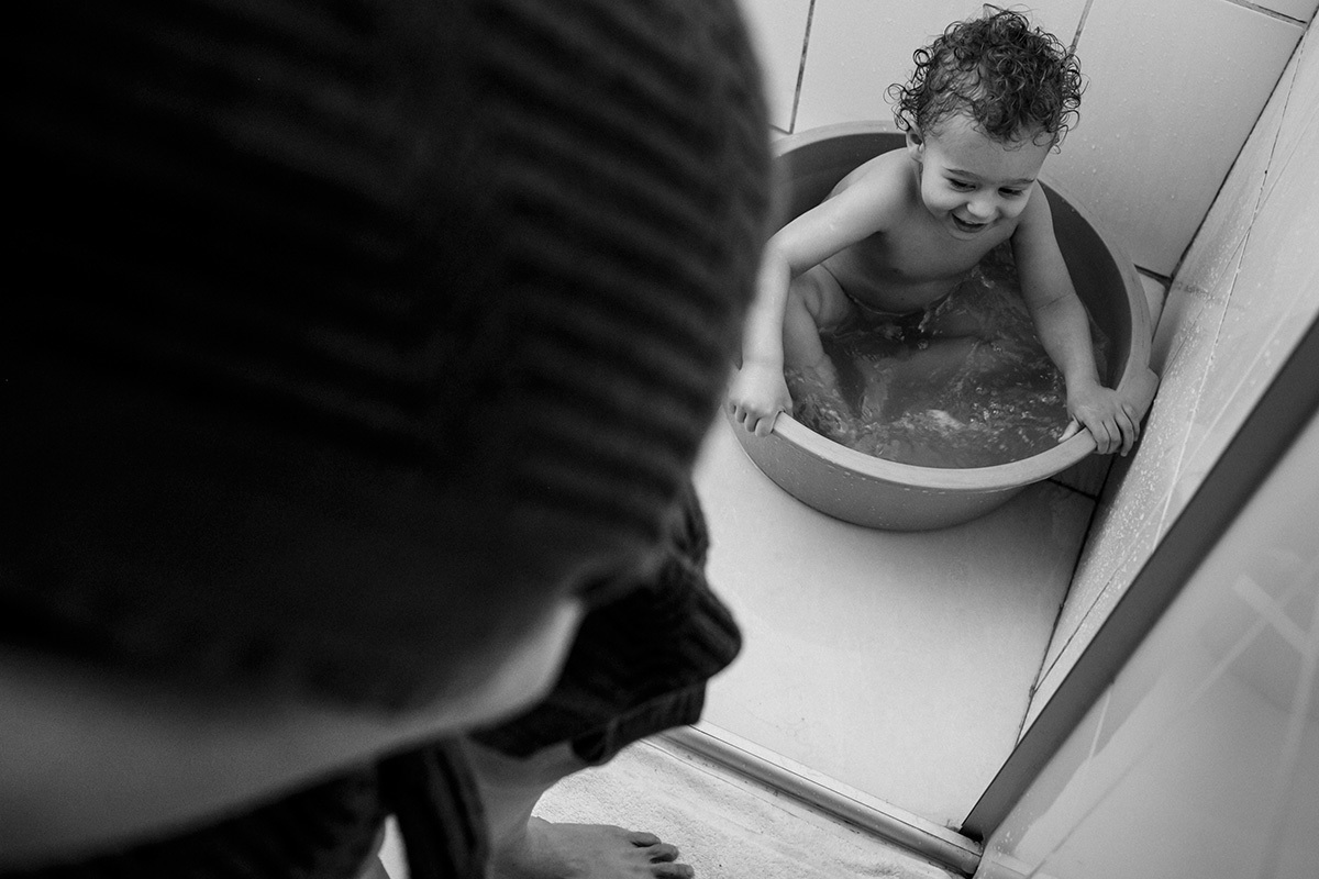 criança brinca na bacia do banho enquanto sua mãe o espera no dia do parto do segundo filho