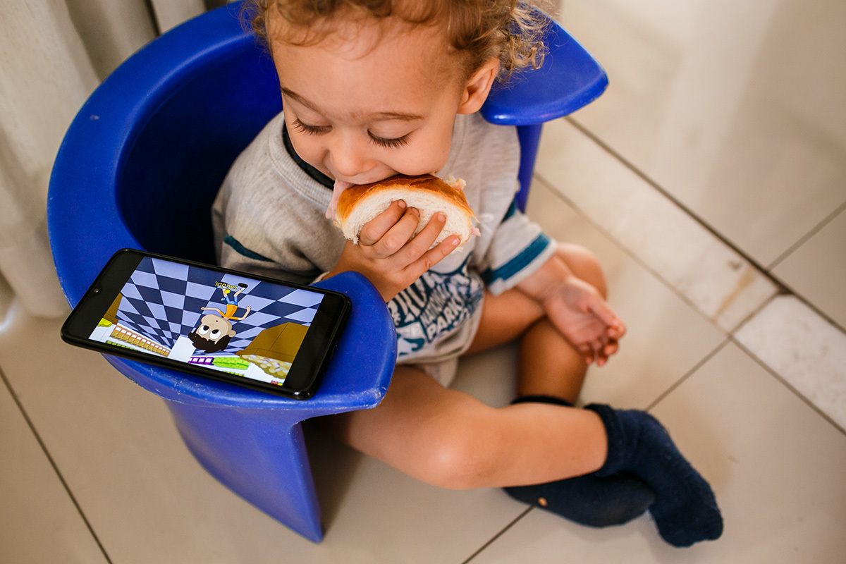 criança lancha e vê celular na banqueta de parto da sua mãe