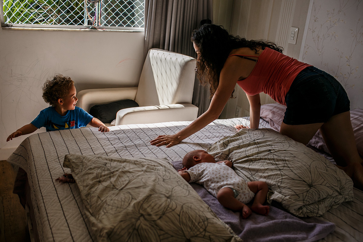 Adriana Costa Fotografou mãe brincando com seu primogênito enquanto seu bebê recém-nascido dorme