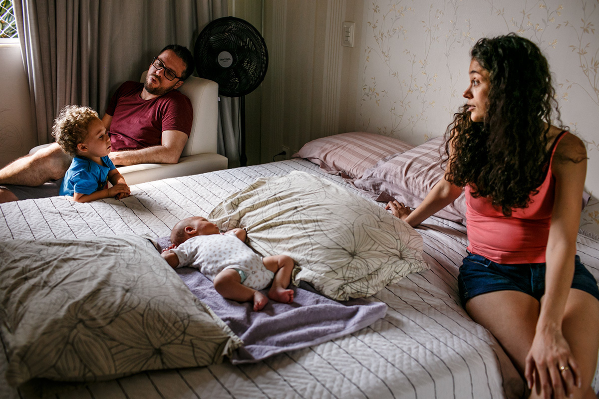 pais conversando com seu filho primogênito enquanto o caçula recém-nascido dorme