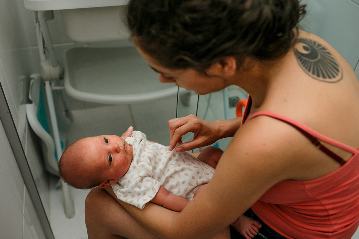 mãe fazendo carinho no seu bebê recém-nascido enquanto a banheira do banho enche de água