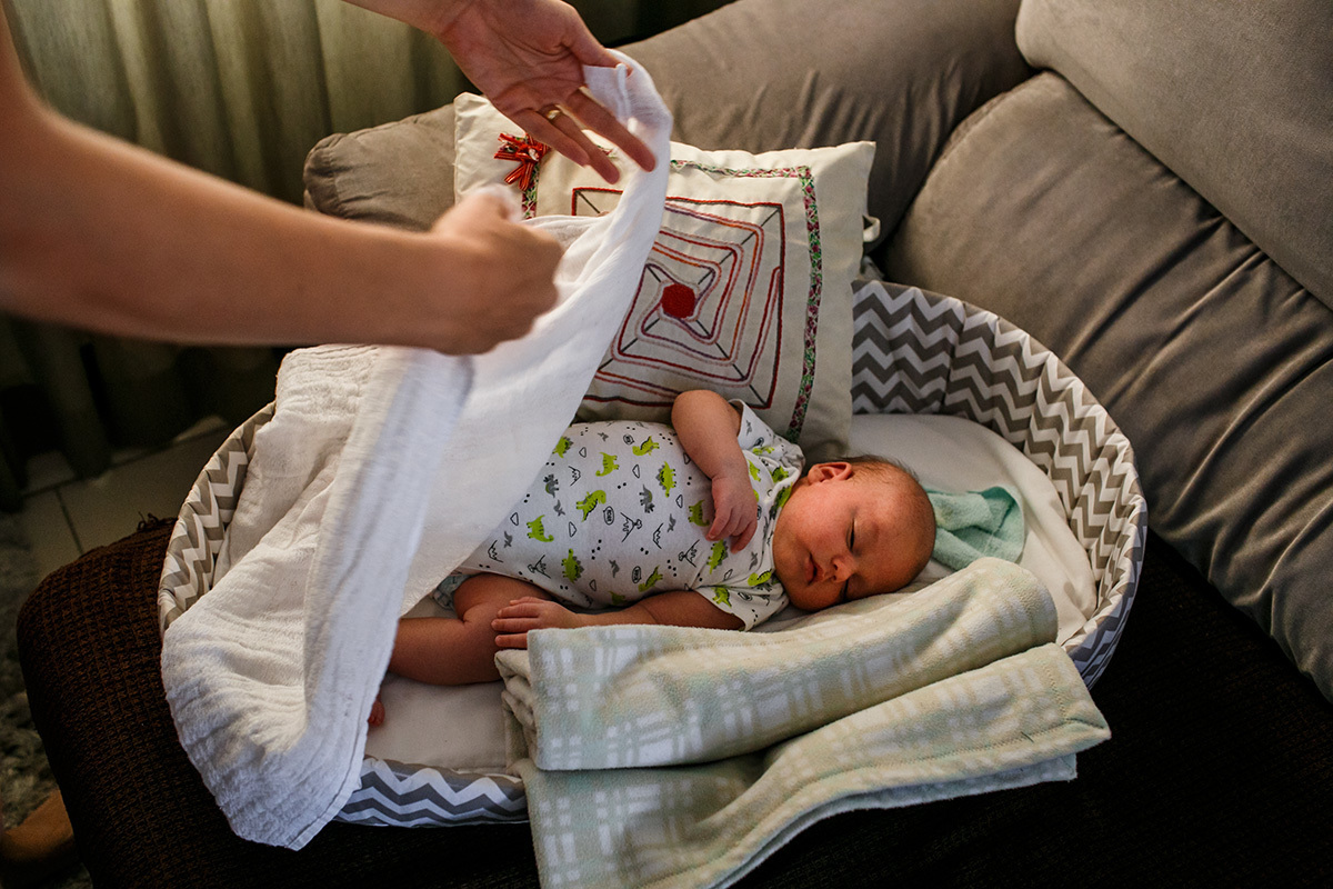mãe colocando seu bebê recém-nascido para dormir no moisés