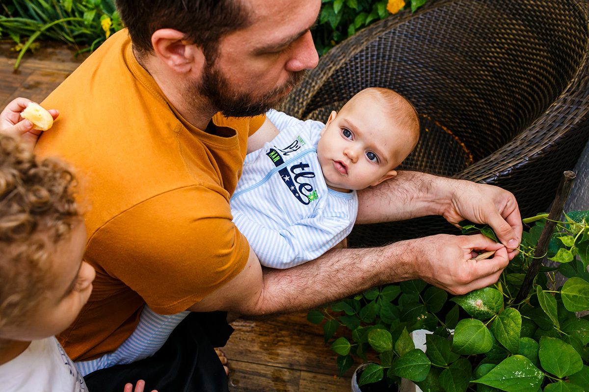 pai com seus filhos colhendo feijão no quintal de casa em foto de Adriana Costa