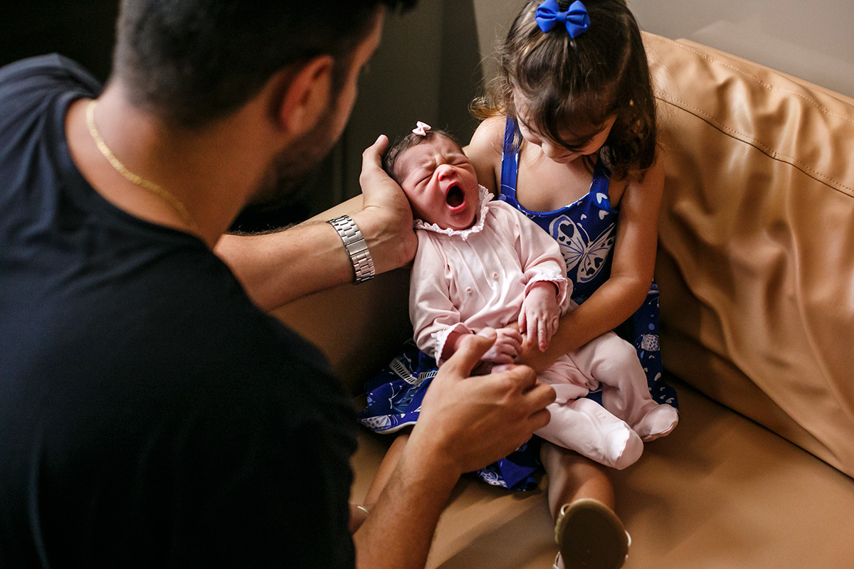 Menina pega sua irmã que acabou de nascer no colo em foto de Adriana Costa