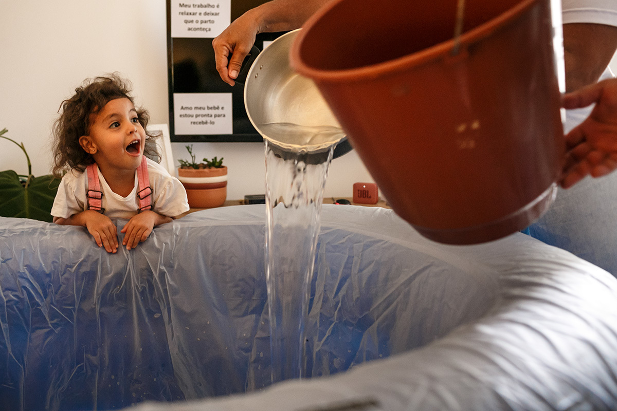 criança admira a banheira sendo enchida com água para o parto de sua mãe 