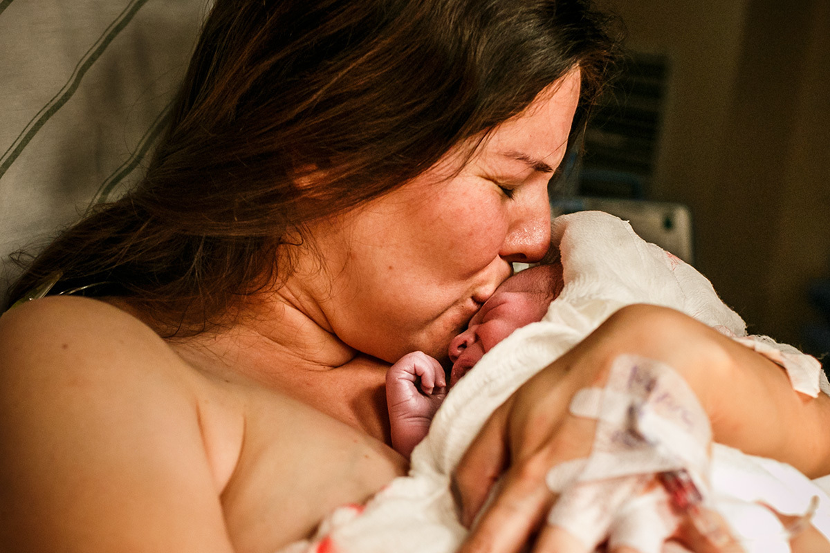 mãe beija emocionada seu bebê que acabou de nascer de parto normal