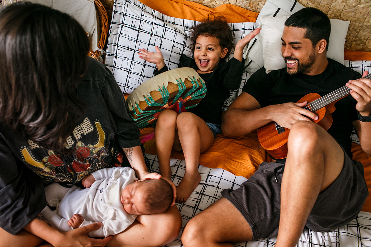 pai toca ukulele e filha tambor para a mãe e o bebê recém-nascido