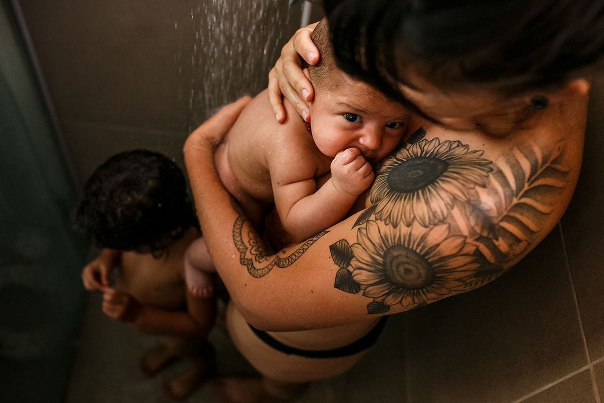 mãe tomando banho de chuveiro com seu bebê e sua filha de 4 anos