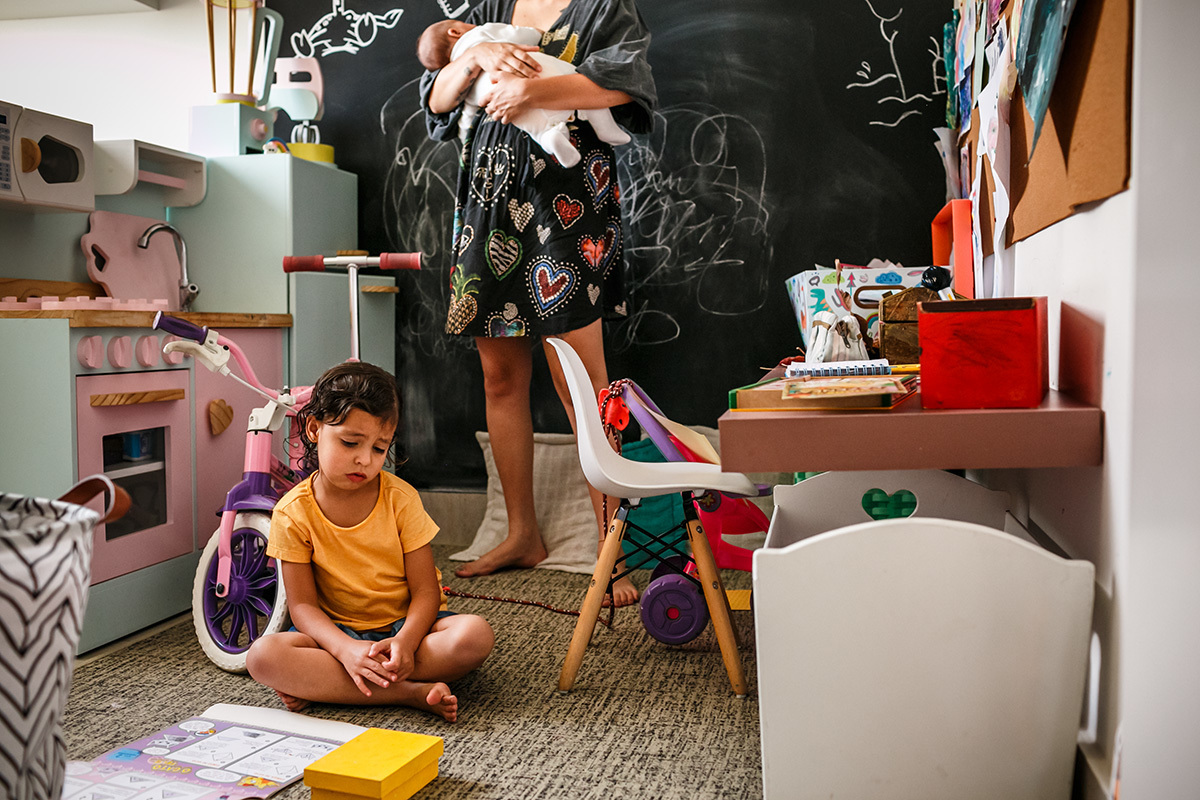 menina emburra chamando a atenção da mãe que está com bebê