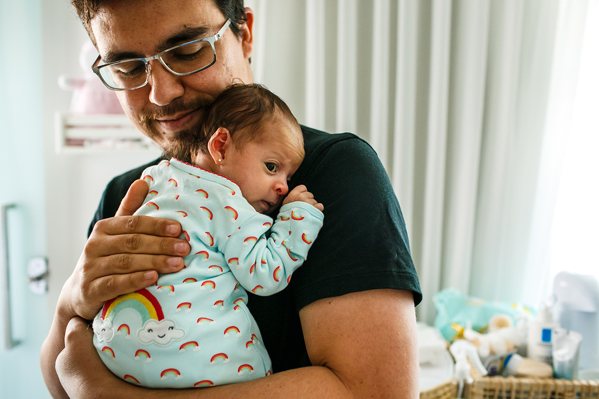 pai carrega com carinho seu bebê recém-nascido em foto de Adriana Costa