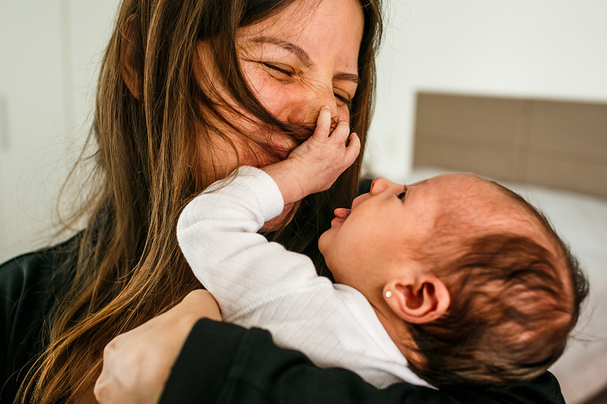 bebê recém-nascido faz careta e puxa o cabelo da mãe em foto de Adriana Costa