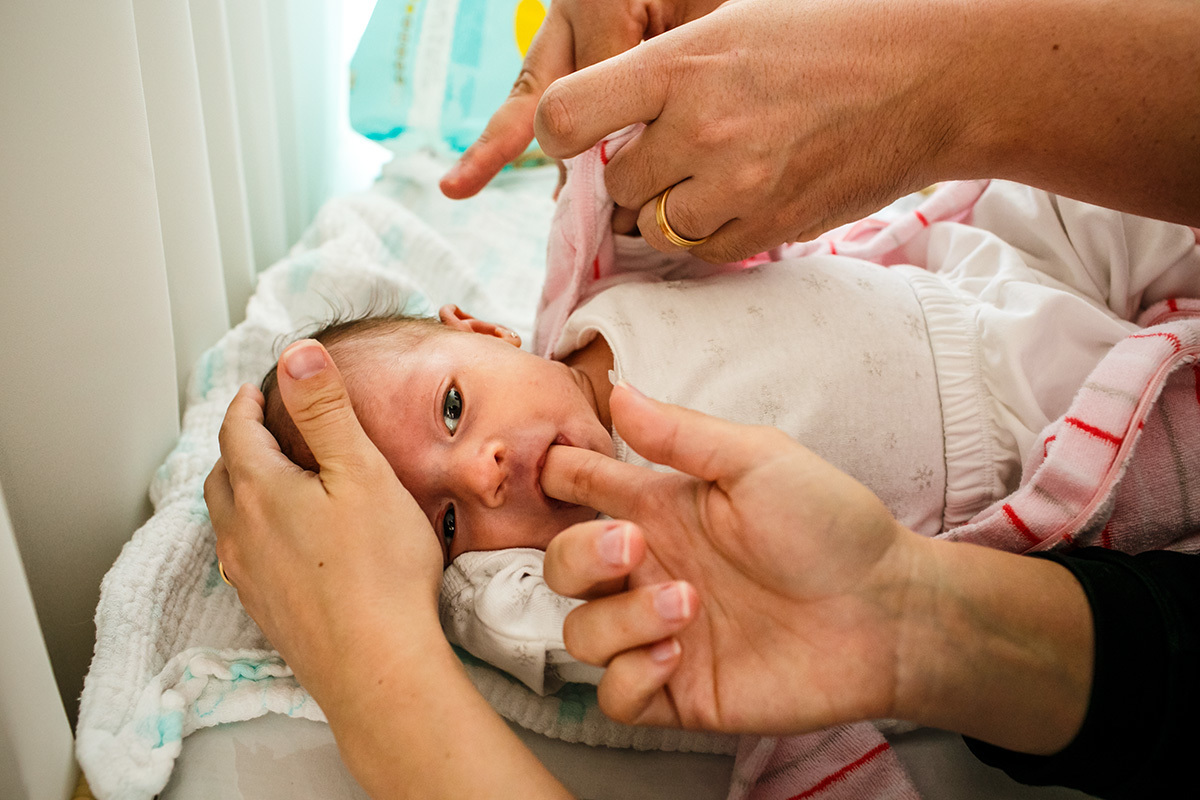 mãe dá o seu dedo para sua bebê recém-nascida chupar e acalmar o choro