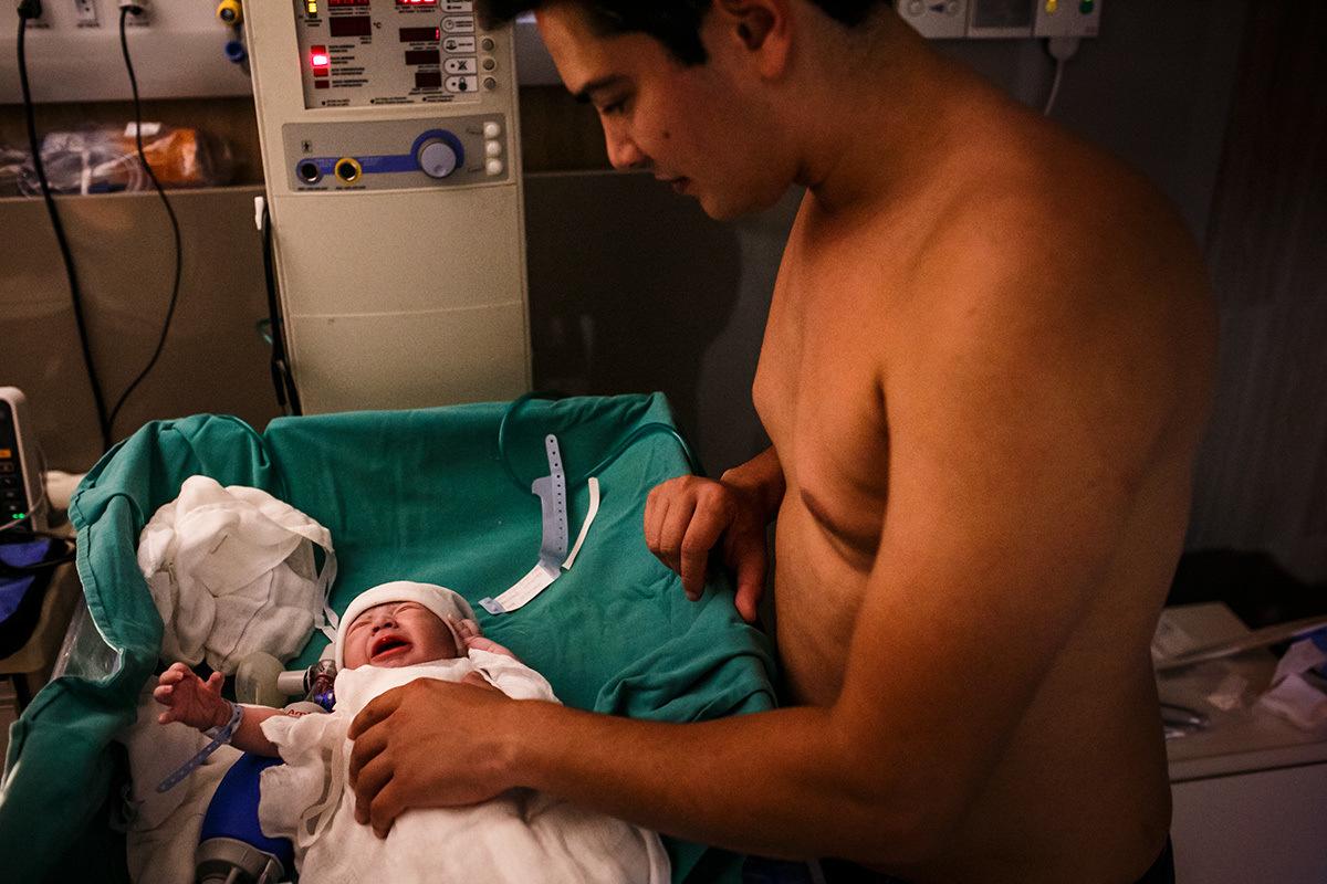 pai se prepara para fazer o contato pele a pele com o seu filho que acabou de nascer em foto de Adriana Costa