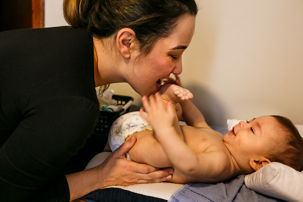 mãe brinca de morder o pezinho do seu bebê enquanto troca a fralda