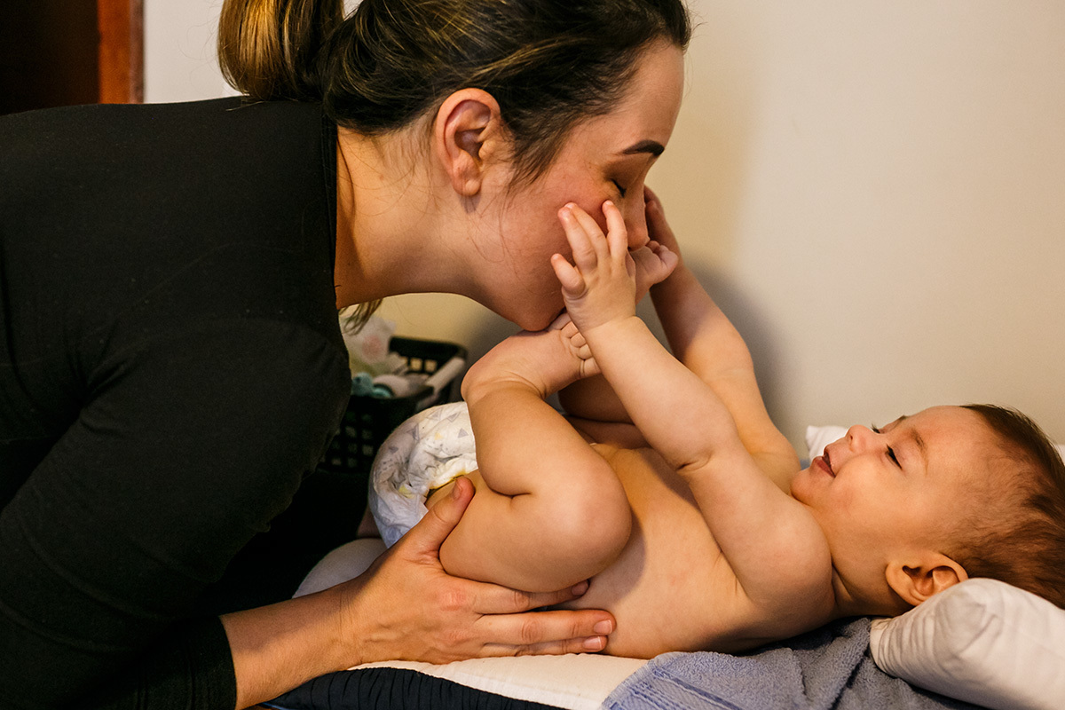 mãe e bebê brincam no trocar de fraldas em foto de Adriana Costa