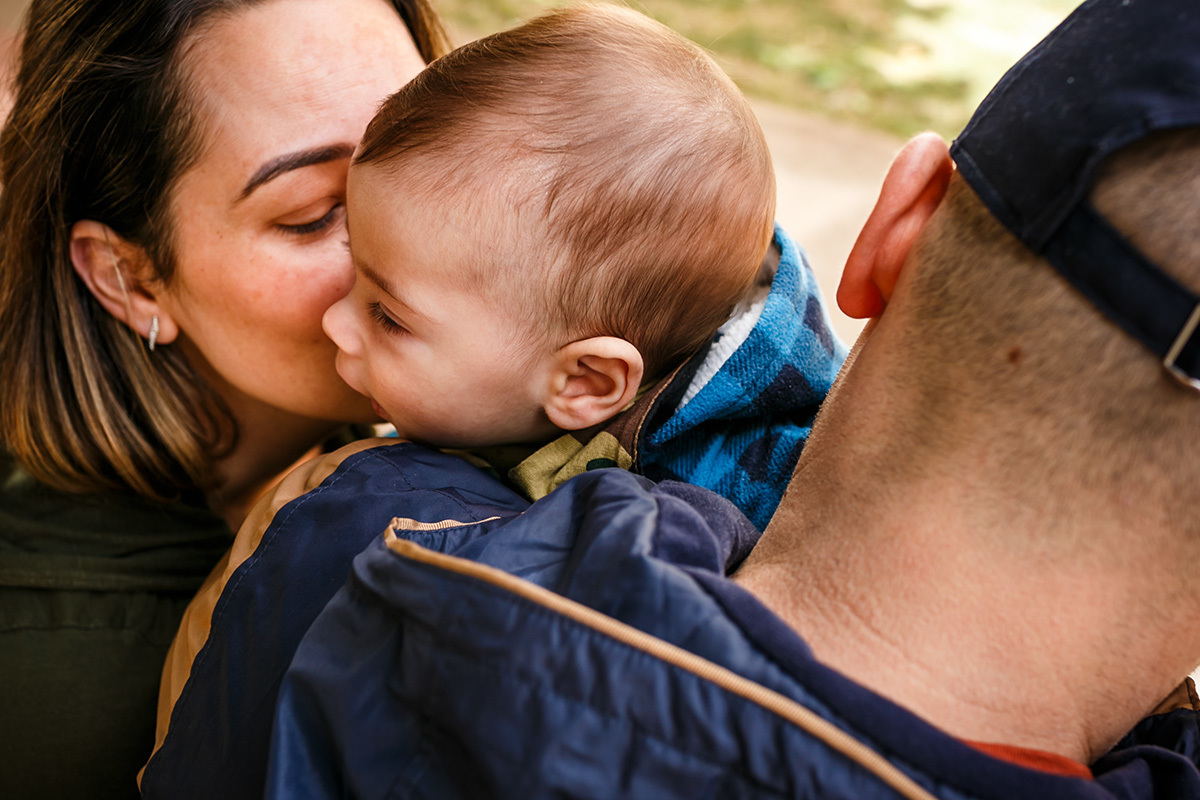 mãe beija seu bebê que está no colo do pai