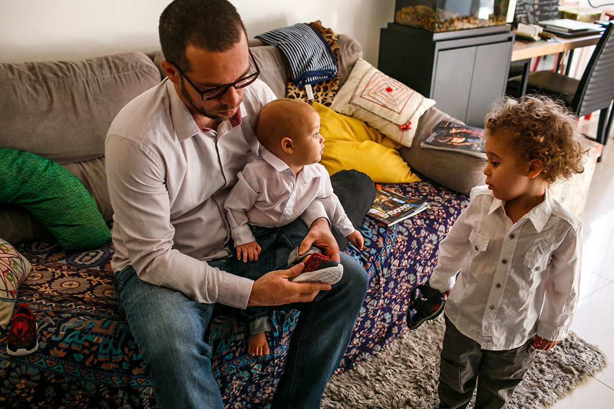 pai ajuda calçando os sapatos nas crianças em foto de Adriana Costa
