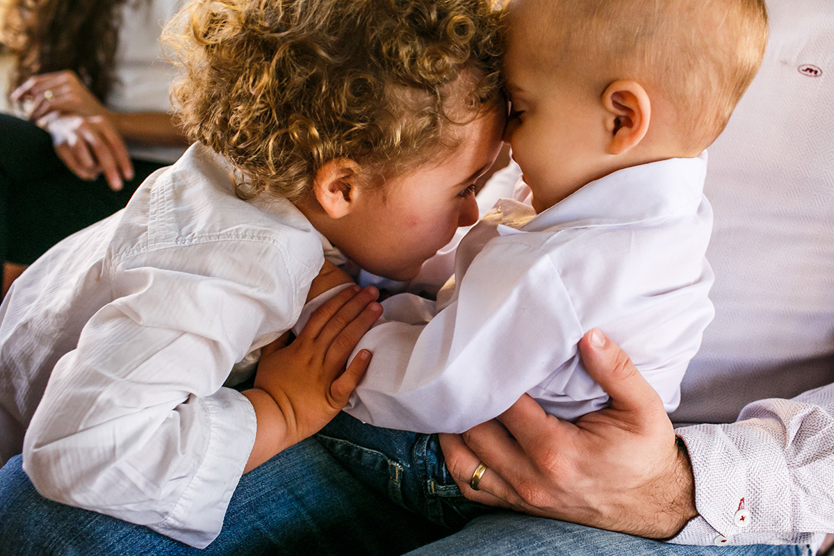 Foto de Adriana Costa do carinho entre irmãos durante o batizado do caçula