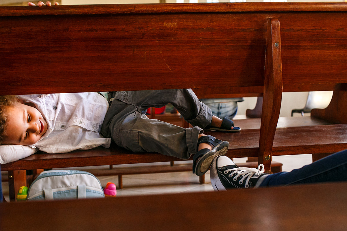 criança brinca com sua tia que está no assento atrás dele na Igreja