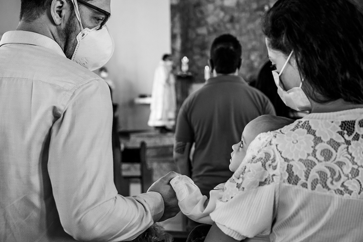 bebê da a mão para o pai durante a missa do batizado em foto de Adriana Costa