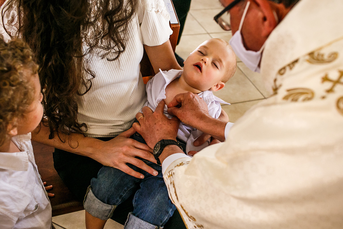 bebê dorme enquanto o padre passa o óleo para ungir 