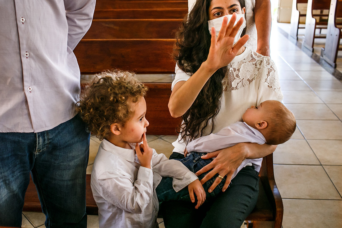 menino observa mãe rezando na missa de batismo do caçula em foto de Adriana Costa