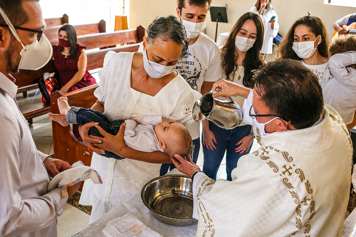 padre derrama a água na cabeça do bebê que dorme na cerimônia de batismo