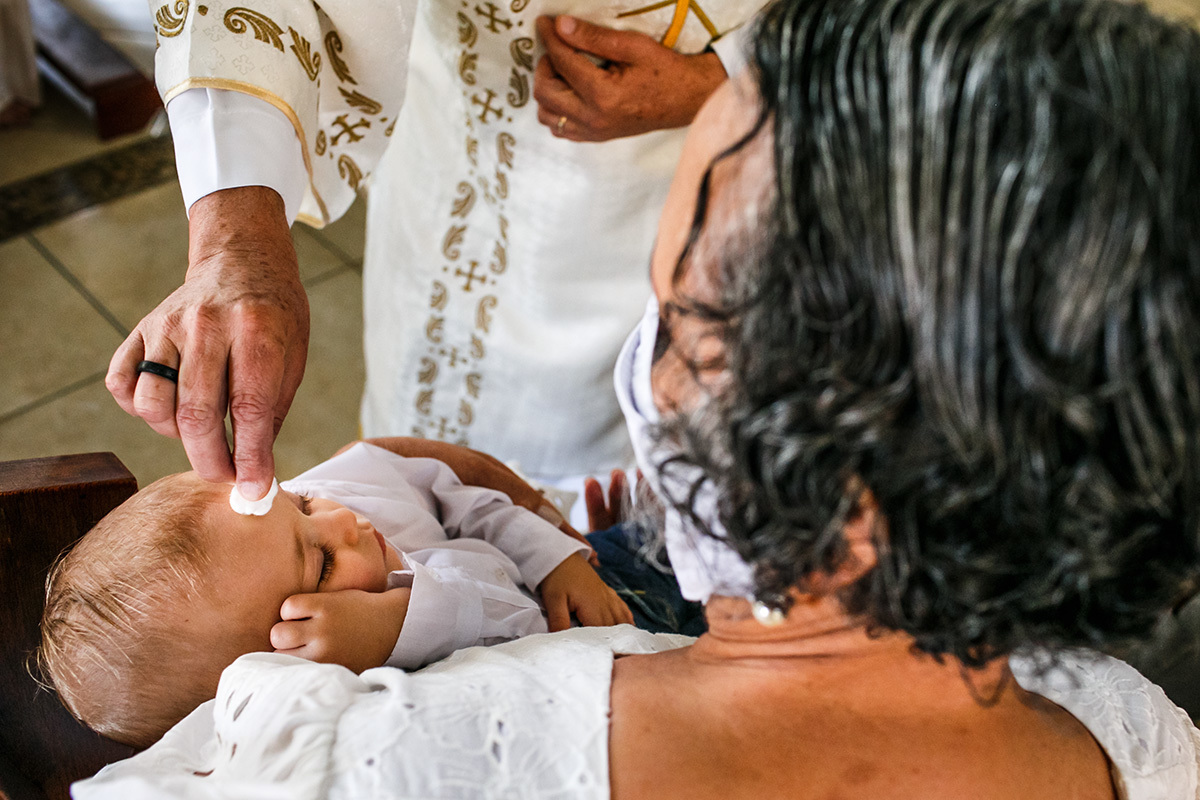 padre passa água benta na testa do bebê que dorme durante o batismo