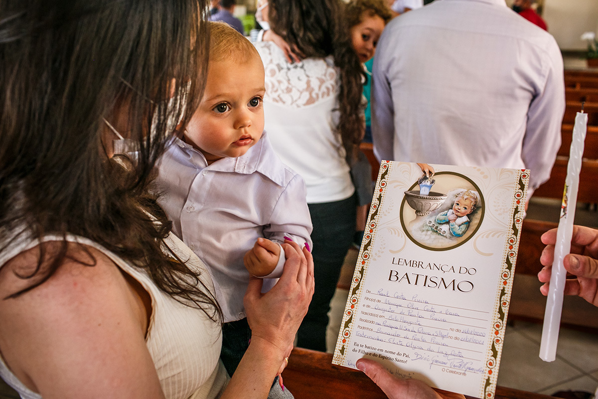 bebê olha o papel do seu certificado de batismo