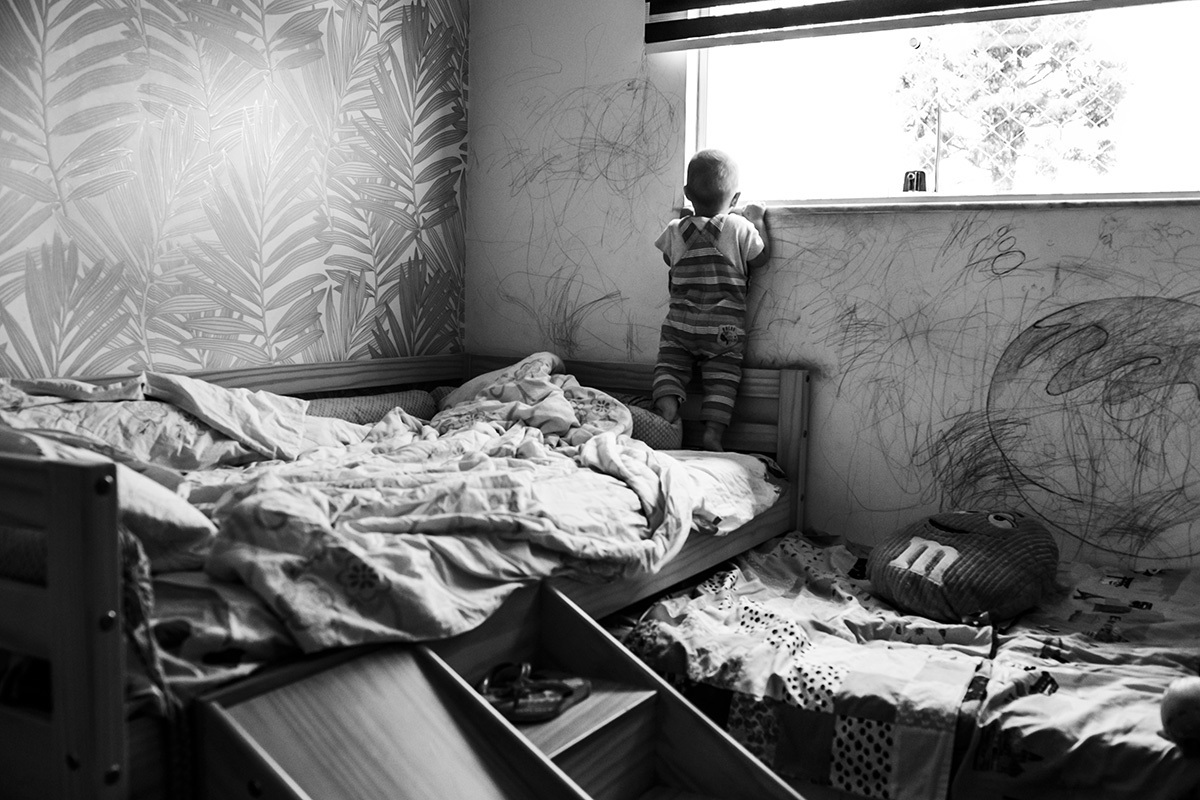 bebê fica na ponta dos pés em sua cama para olhar a janela 