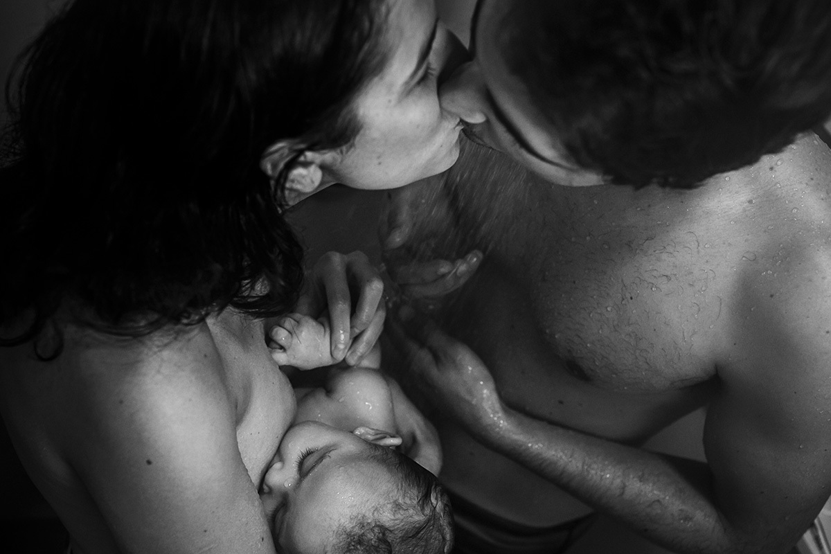 bebê amamentando no banho de chuveiro com os seus pais em foto de Adriana Costa