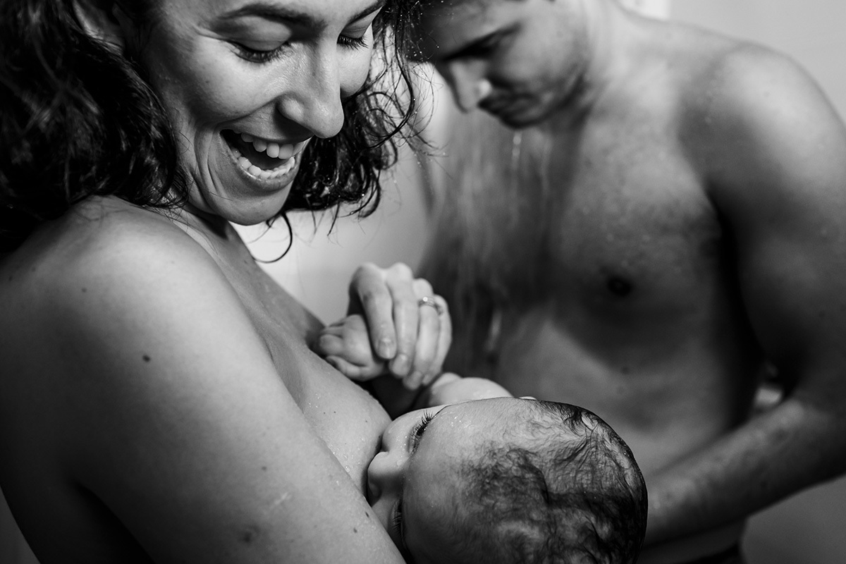 pai dá o banho no chuveiro na sua bebê enquanto ela amamenta