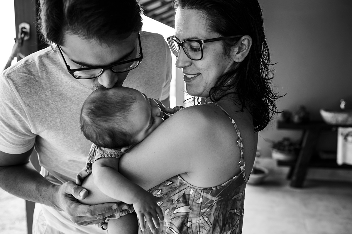 pai beija sua bebê que dorme no colo da mãe