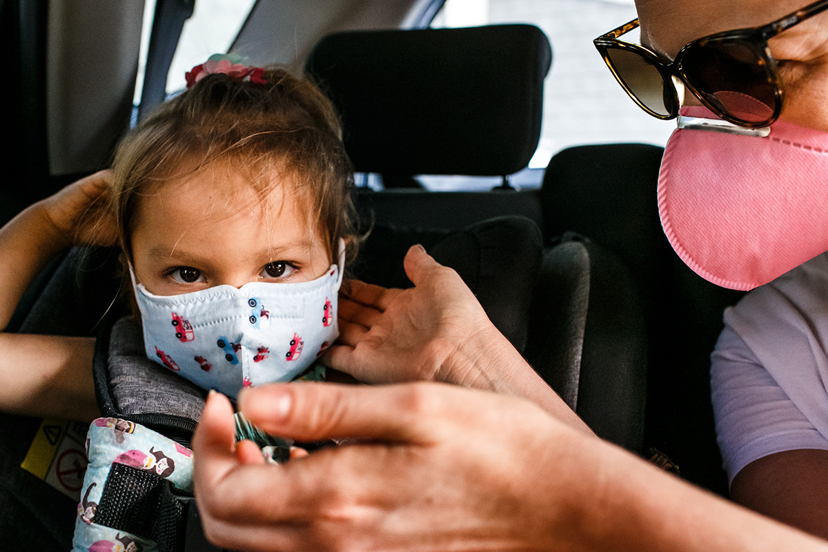 mãe colocando mascara na filha para passear