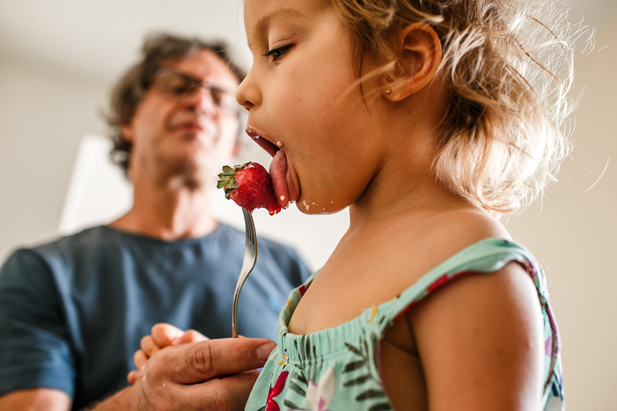 menina lambe o morango que o pai oferece em foto de Adriana Costa