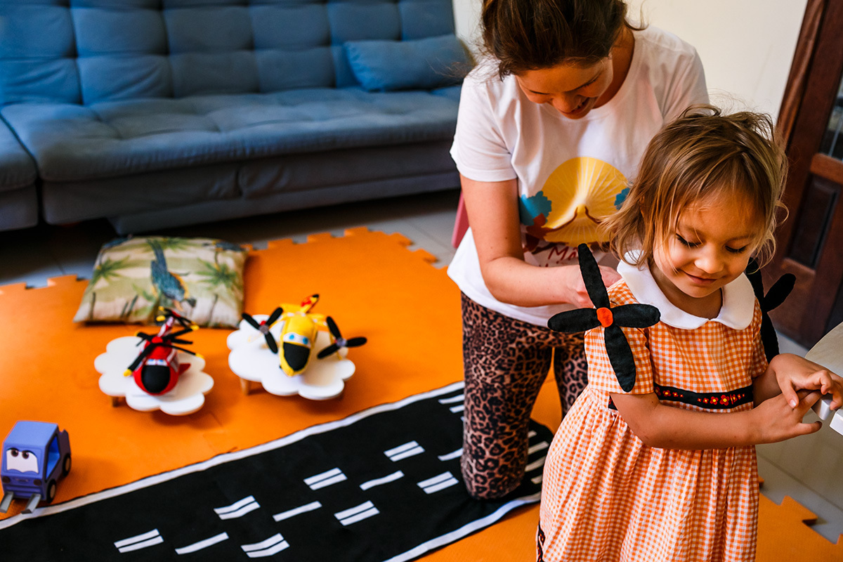 mãe coloca vestido na filha com hélices nos ombros para a sua festa em casa de aniversário com o tema Aviões da Disney Pixar