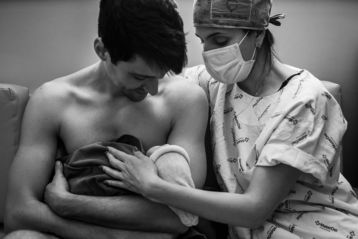 obstetra abraça pai e bebê com carinho após o nascimento